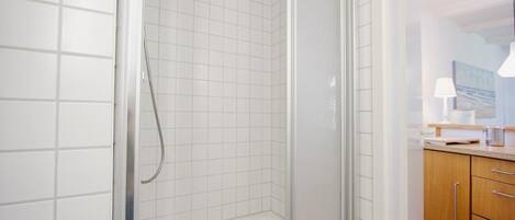 A modern bathroom with white tiled walls, a glass shower enclosure, and wooden cabinets.