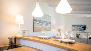 A modern kitchen with wooden countertops, pendant lights, and a view of the ocean through a window. - Small hideaway<br>- A very special domicile in the middle of Friedrichstrasse -<br>The large double bed (180x200, mattress size approx. 1.92 m x 90 cm) is located in the modern living room, separated by a room divider. The flat screen TV. (Westerland)