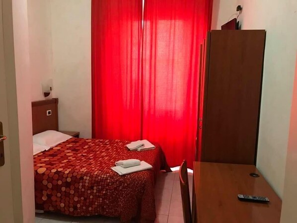 A small, neatly arranged bedroom with a single bed, a wooden wardrobe, and a desk with a remote control. - Les Artes (Rome)