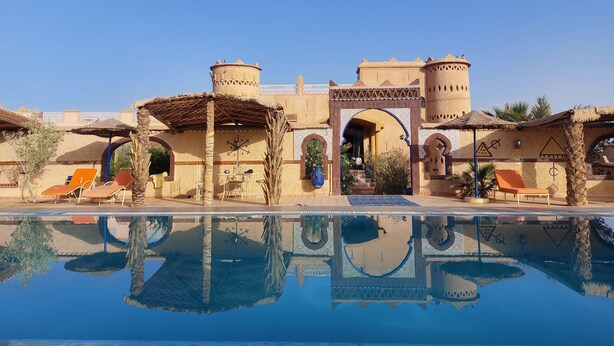 A pool with a reflection of a building with arches and towers. - Dar Tafouyte (Taouz)
