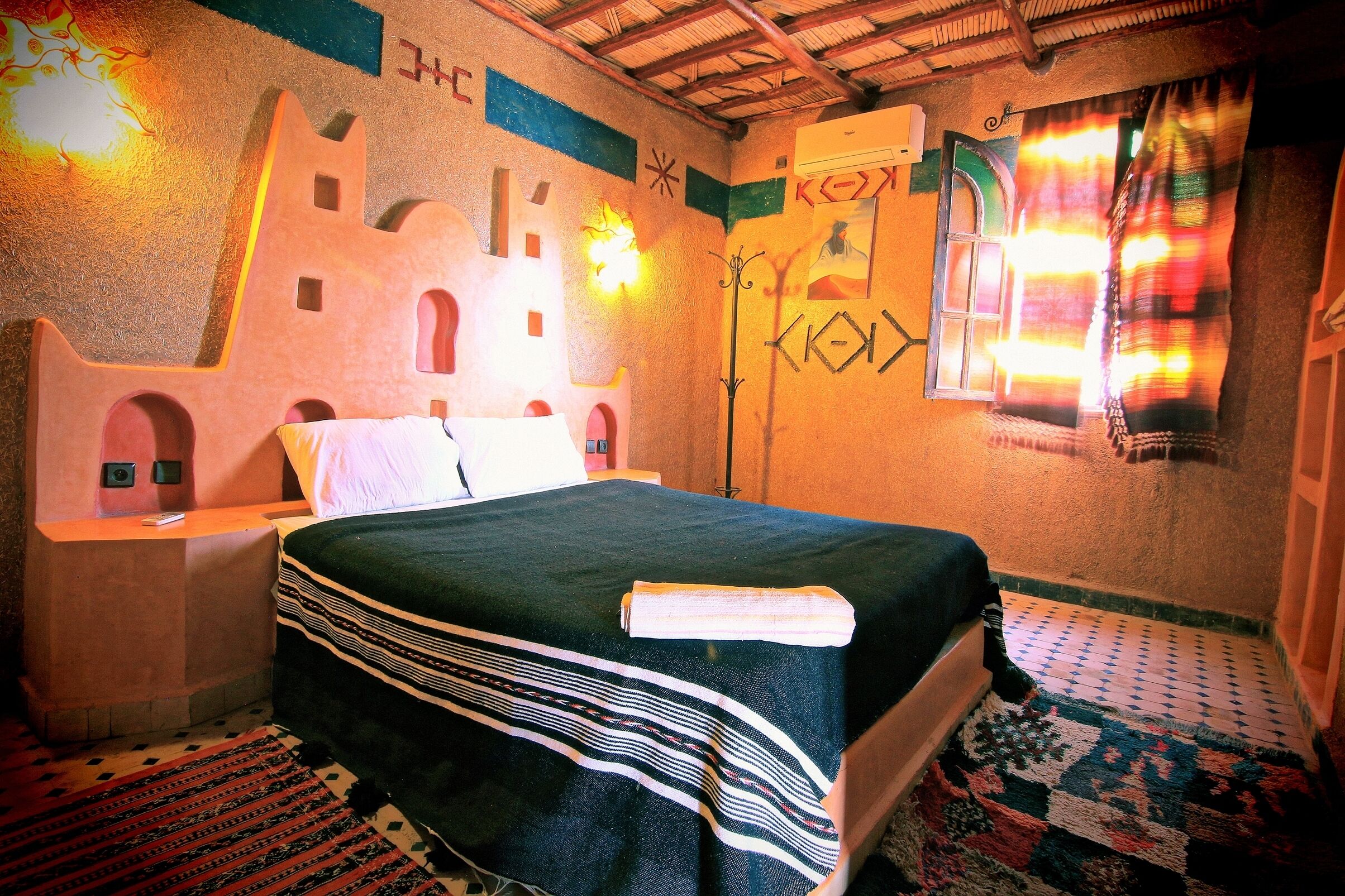 Un dormitorio con cama, mesitas de noche, alfombra estampada y una pared con detalles decorativos.