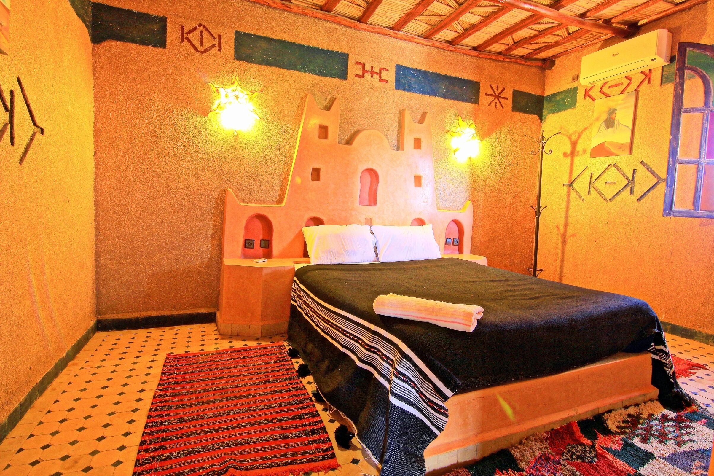 Ein Zimmer mit einem Bett, einem gemusterten Teppich und einem Wandbild.