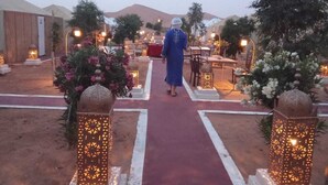 A person walking down a pathway lined with lanterns and floral arrangements, leading to a building with tables and chairs set up outside. - Dar Tafouyte (Taouz)
