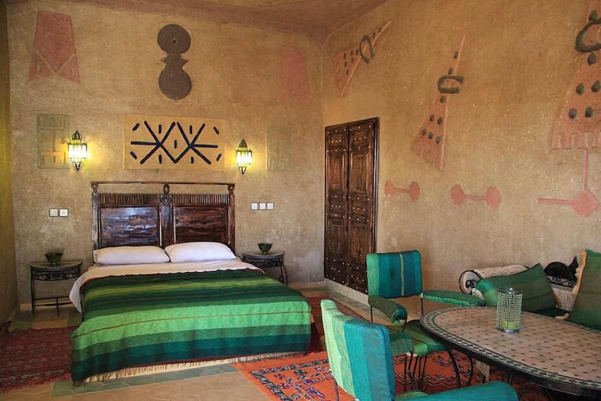 Una habitación con una cama, dos mesitas de noche, un sofá verde, una mesa redonda y una pared con diseños decorativos.