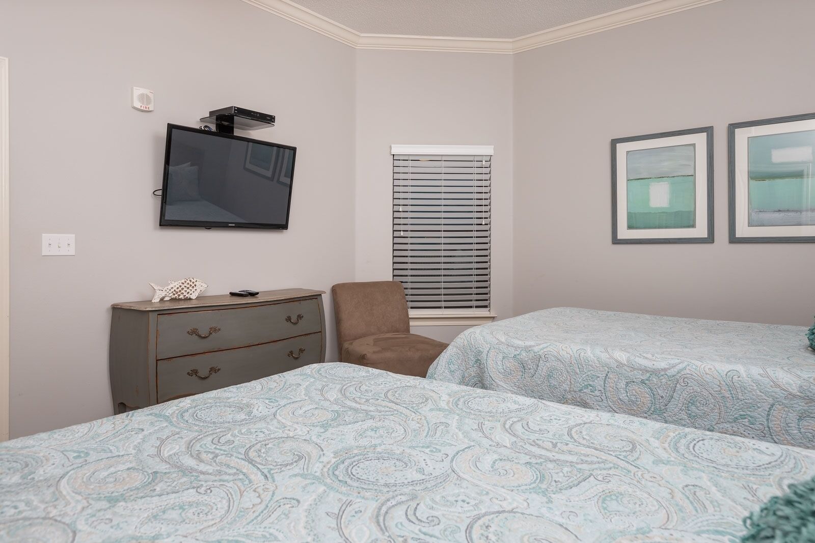 A bedroom with two beds, a dresser, a chair, a TV, and two framed pictures on the wall.