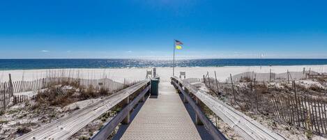 A wooden boardwalk leading to a beach with a flag on a pole.