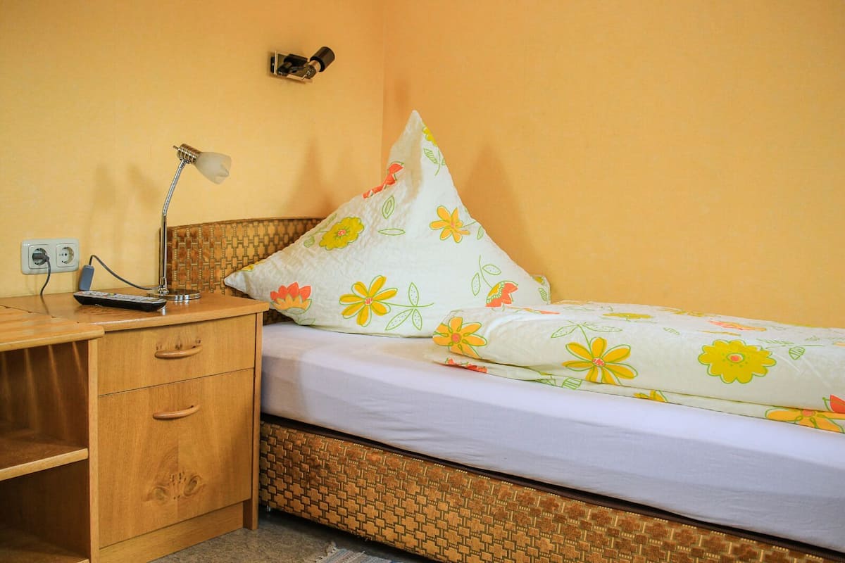 Une chambre avec un bureau en bois, une lampe, un lit avec une literie à motifs floraux et un interrupteur fixé au mur.