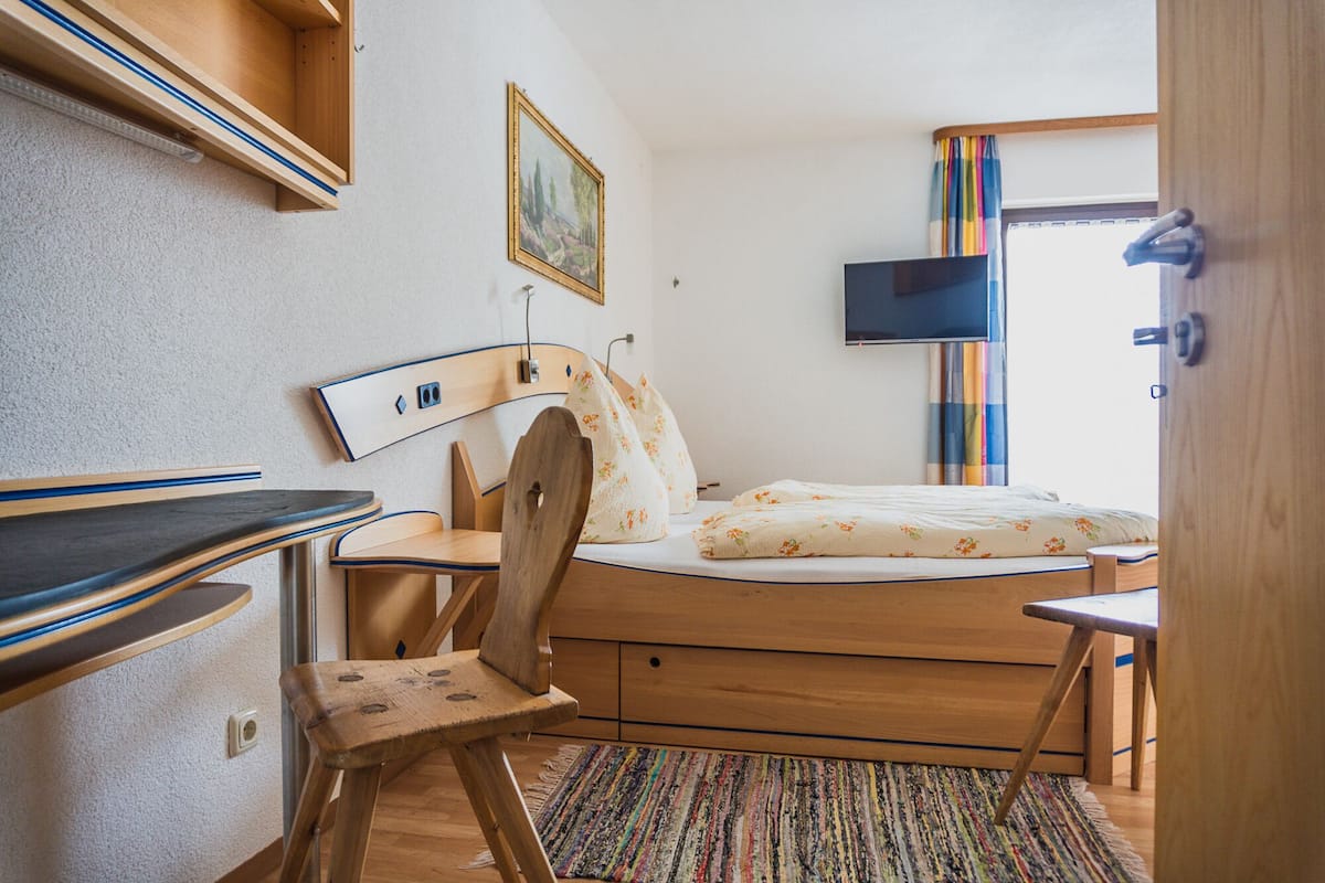 Une chambre à coucher comprenant un lit, un bureau en bois, une chaise et un téléviseur fixé au mur.