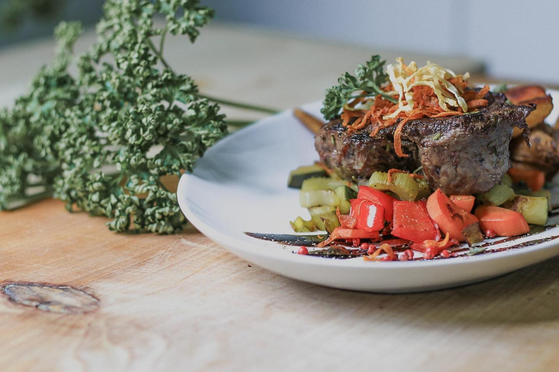 A plate with a steak topped with vegetables and a sprig of parsley.