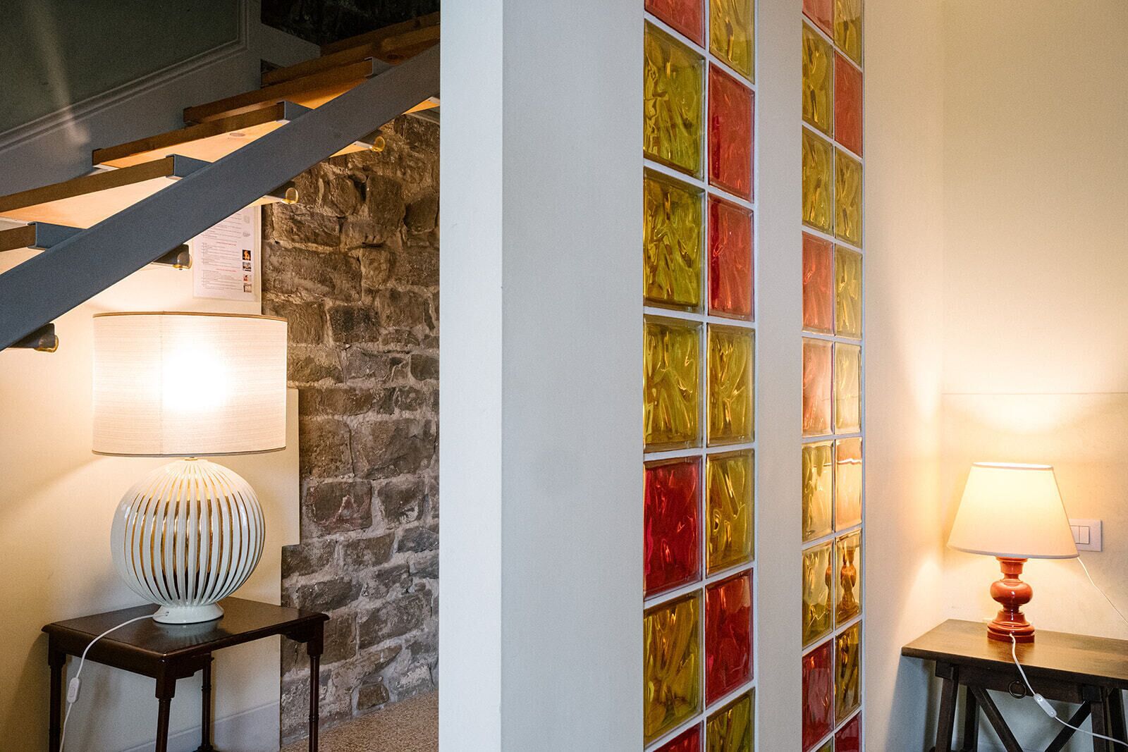 A staircase with a stone wall, two lamps on tables, and a colorful glass wall.