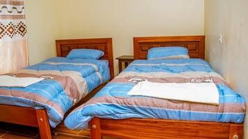 Two wooden beds with blue and brown bedding, a small bedside table, and a patterned curtain.