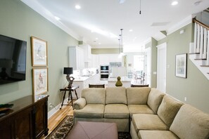 A modern living room with a sectional sofa, a flat-screen TV, and a dining area with a kitchen in the background.