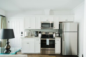 Une cuisine moderne avec des meubles blancs, un réfrigérateur en acier inoxydable, un four à micro-ondes, une cuisinière et une machine à café.