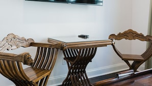 Een houten bank met een leeuwenkop ontwerp, een tafel met glazen blad en een aan de muur bevestigde televisie.