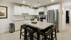 A modern kitchen with white cabinets, stainless steel appliances, and a central island with bar stools. - Plunge Pool and Parking, 3 Stories in Historic Downtown by Lucky Savannah (Savannah)