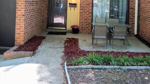 A two-story building with a yellow exterior, a glass door entrance, and a patio area with a table and chairs. - Quiet Townhome in central Raleigh (Raleigh)