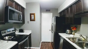 A compact kitchen with dark wooden cabinets, a microwave, a stove, a sink, and a refrigerator. - Quiet Townhome in central Raleigh (Raleigh)