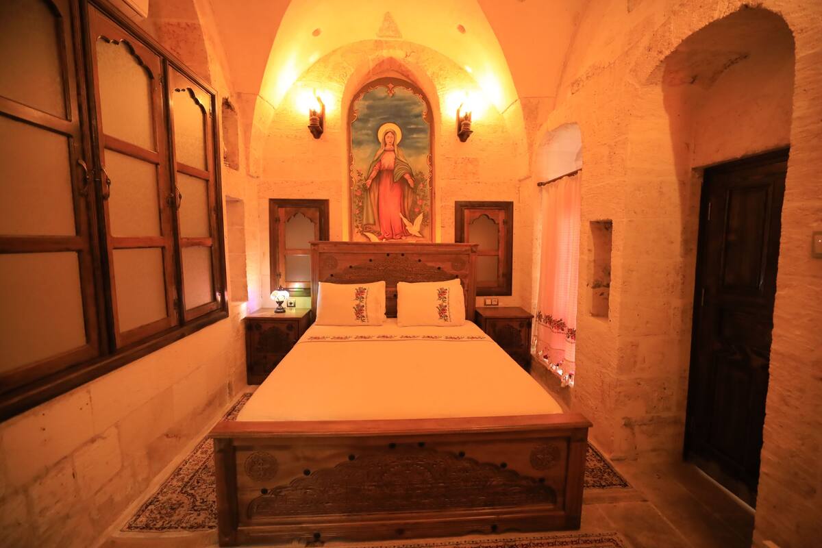 Ein traditionell eingerichtetes Zimmer mit einem hölzernen Bett, einem religiösen Gemälde darüber und einer Steinwand.