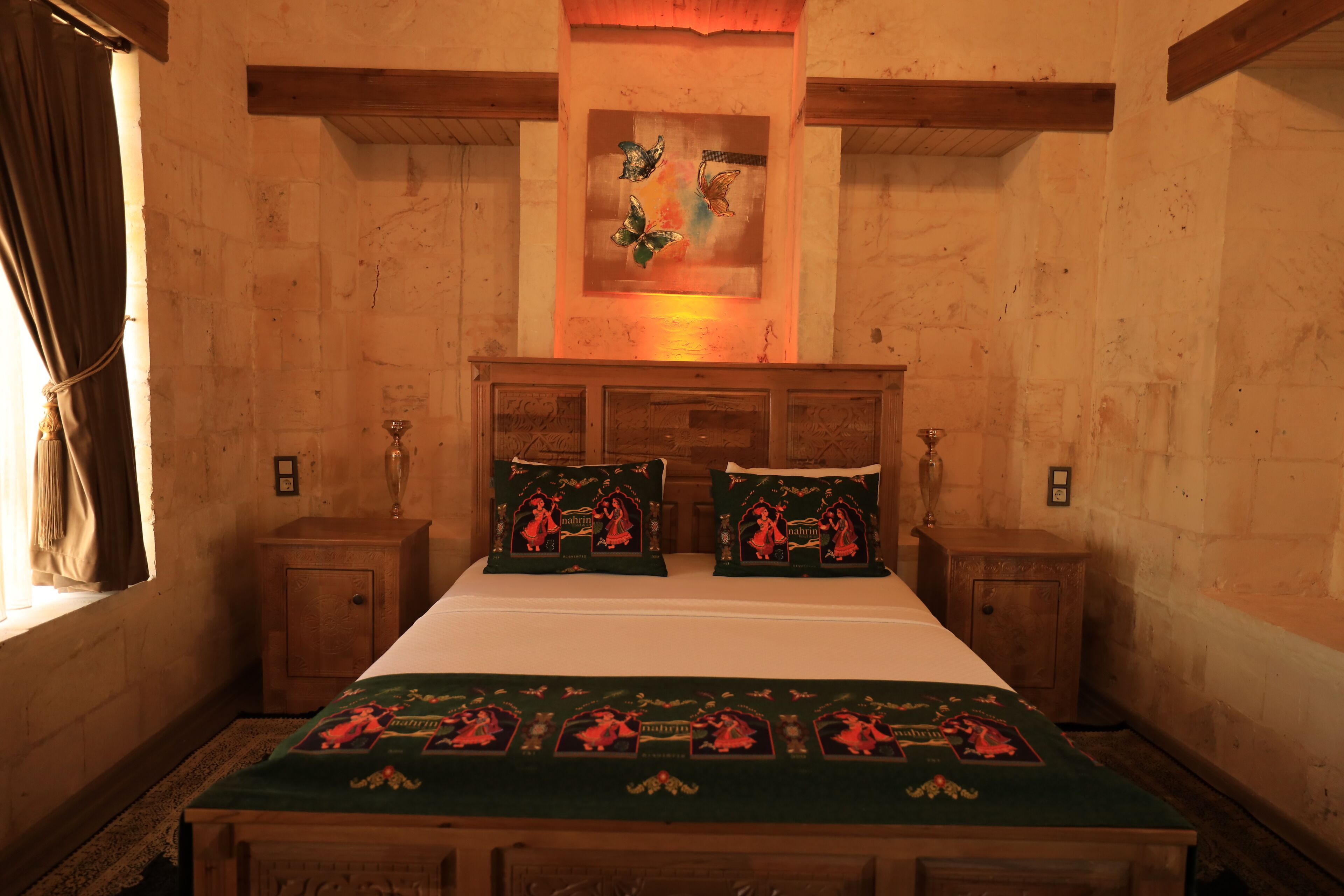 Un dormitorio con cabecera de madera, una cama con ropa de cama verde, dos mesitas de noche y una obra de arte colgada en la pared sobre la cama.