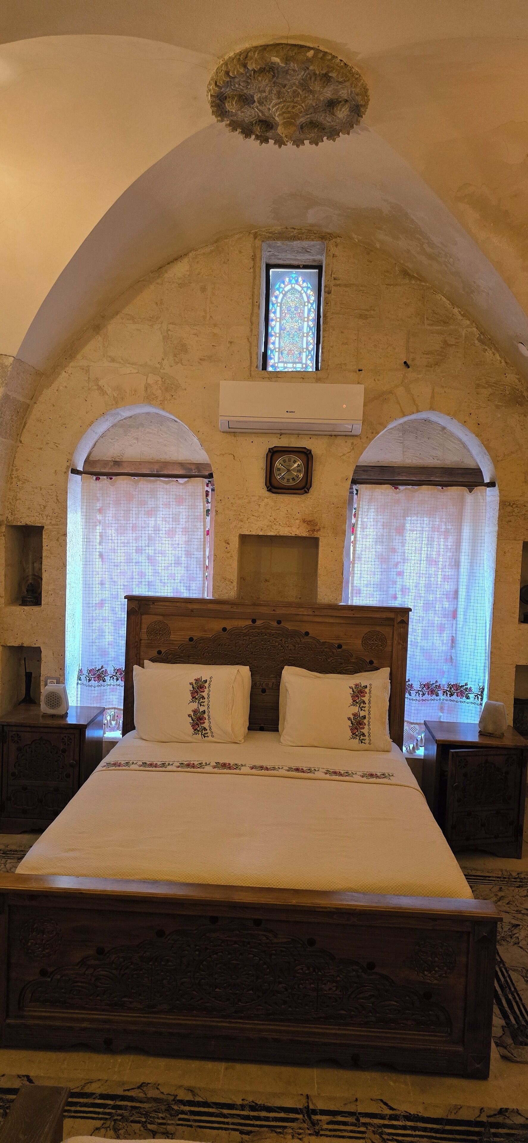 Un dormitorio con una cama grande, ventanas en arco, cabecera de madera y techo decorativo.