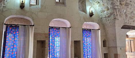 A room with a high, textured ceiling, small windows with patterned curtains, and a bed with a floral bedspread.