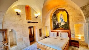 Ein Schlafzimmer mit einem großen Bett, Steinwänden und einem religiösen Gemälde über dem Bett.