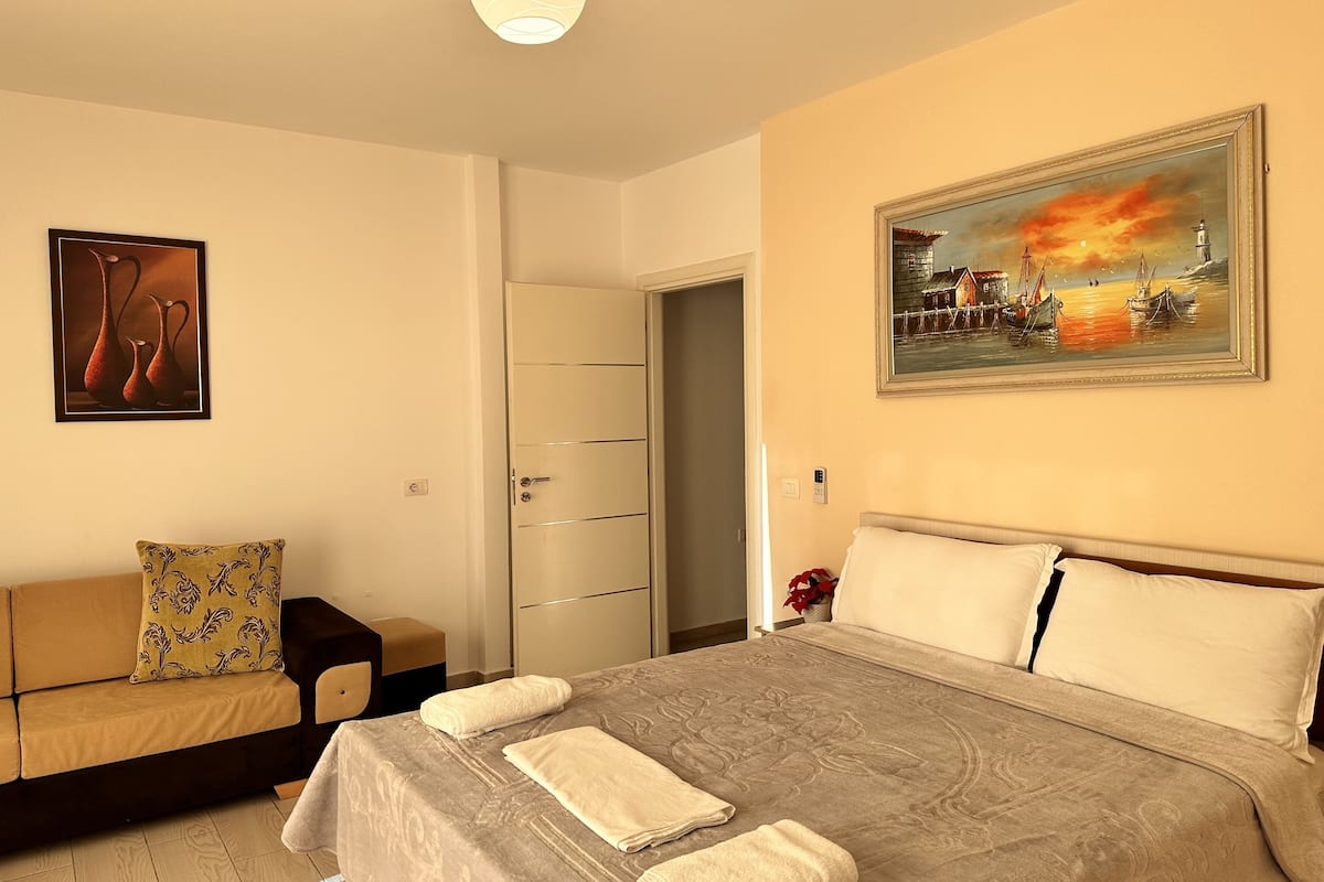A bedroom with a bed, a sofa, a painting, and a door.
