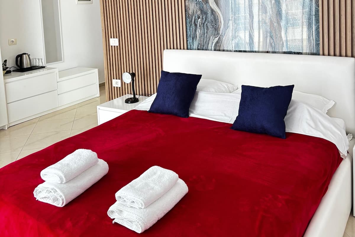 A modern bedroom with a large bed, white bedding, a red throw, and a marble wall art piece.