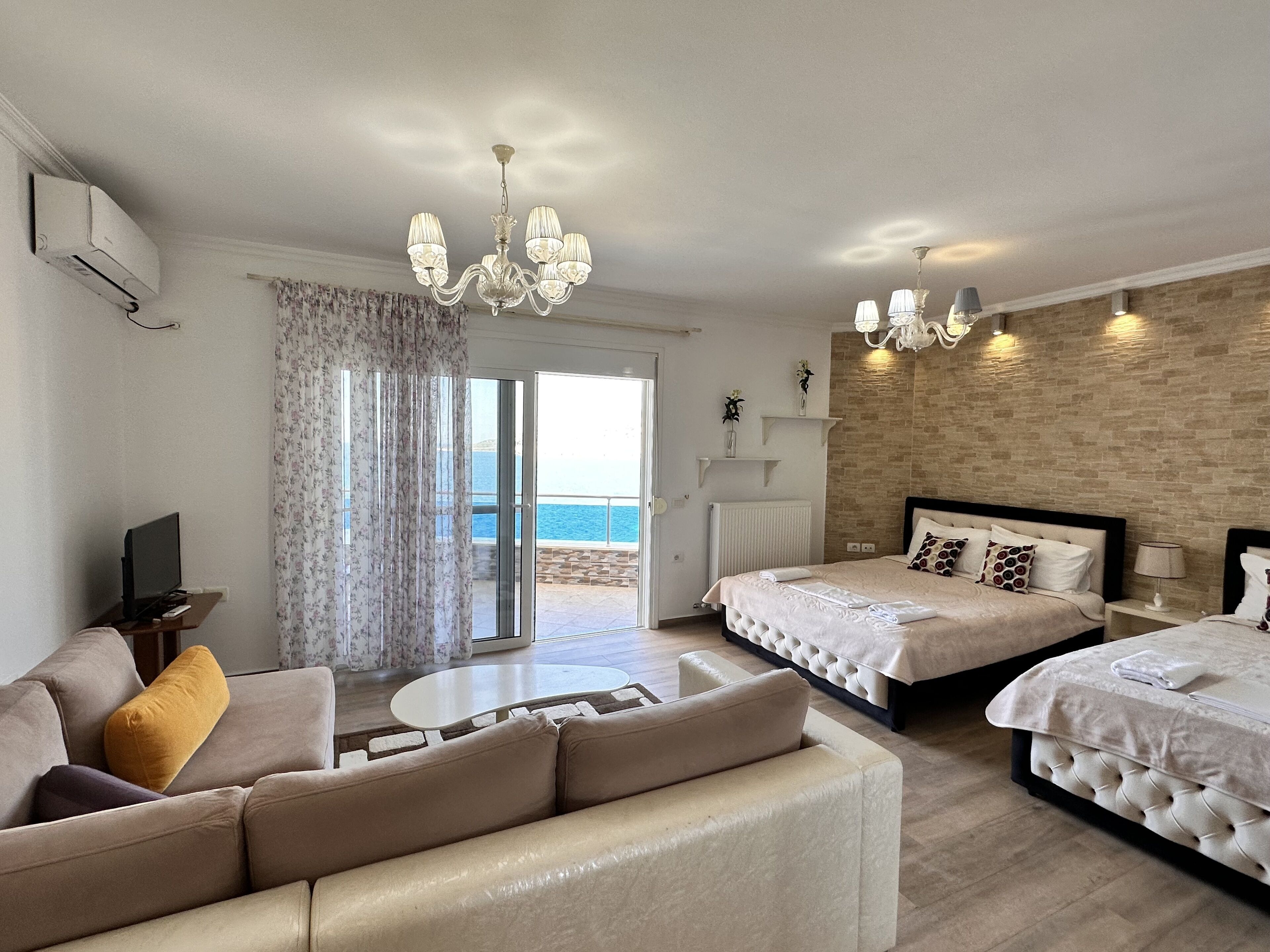 A hotel room with a sofa, two beds, a TV, a table, and a view of the sea.