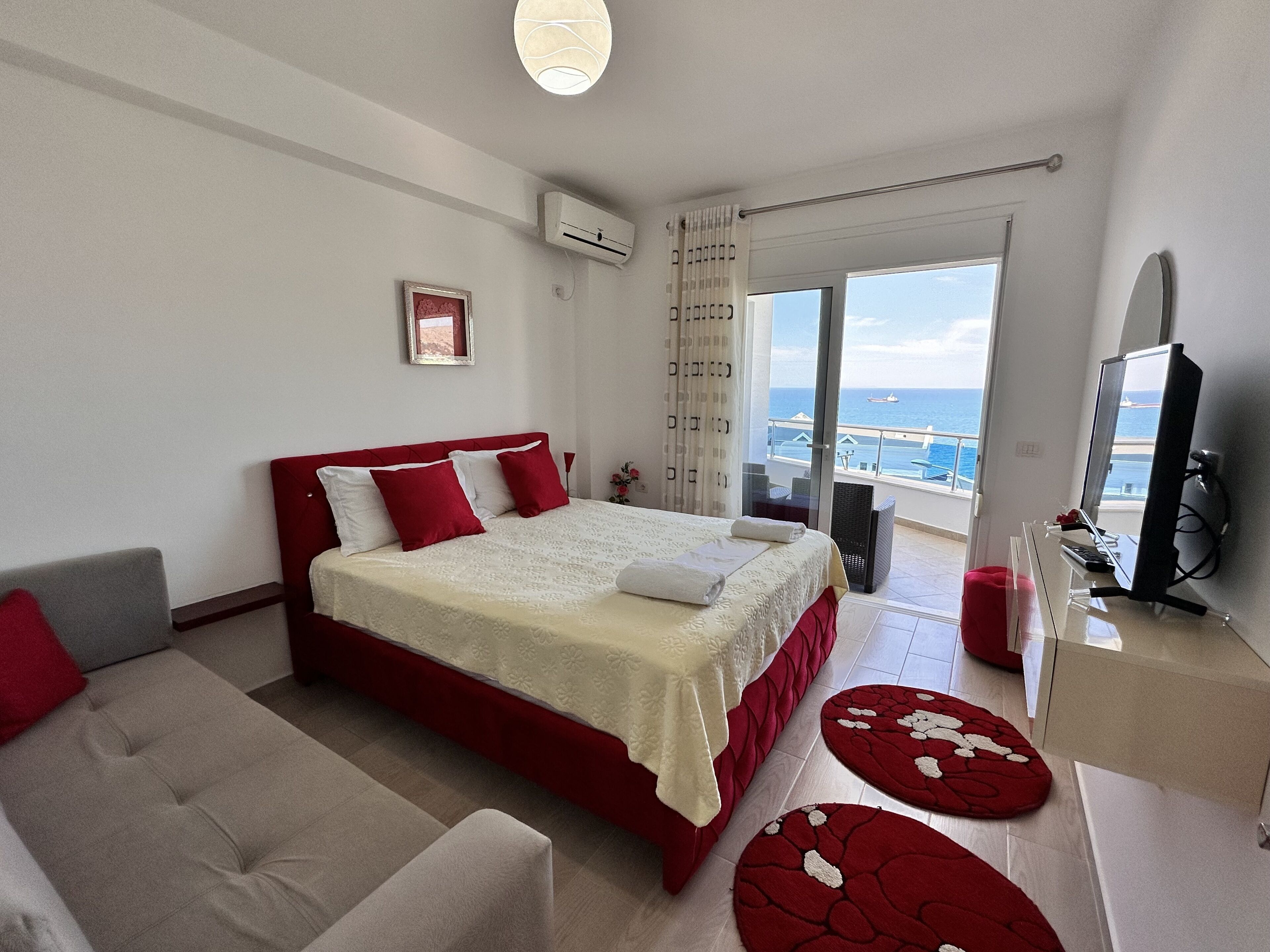 A bedroom with a bed, a sofa, a TV, and a balcony with a view of the sea.
