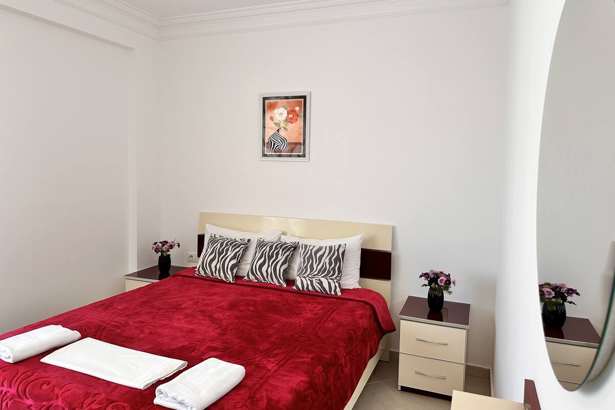 A neatly arranged bedroom with a large bed, a bedside table, a dresser, and a mirror.