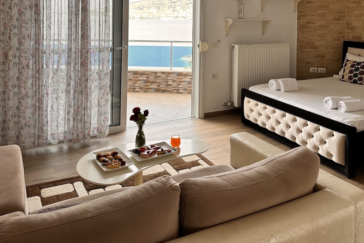 A modern bedroom with a bed, a sofa, a coffee table, and a view of the sea.