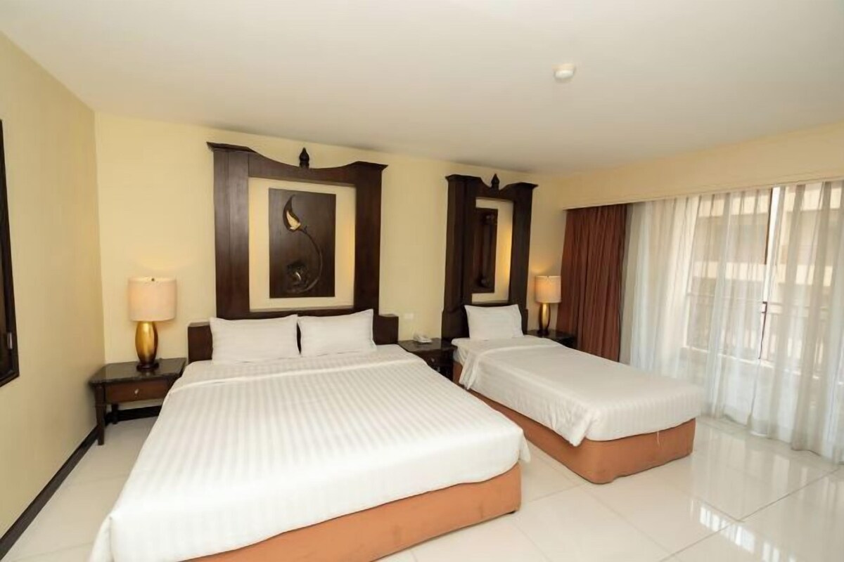 A hotel room with two beds, a large mirror, and a view of the outdoors through sheer curtains.
