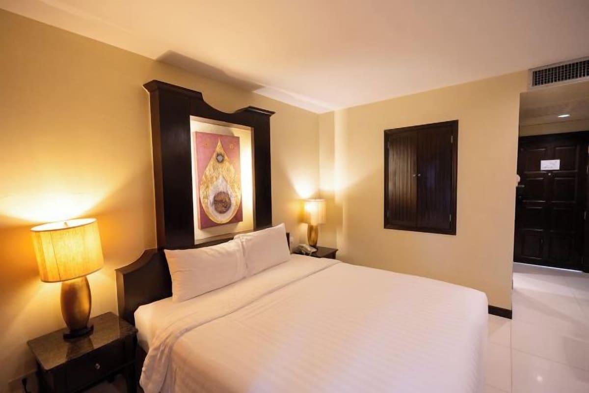 A hotel room with a large bed, two bedside lamps, a nightstand, and a framed artwork on the wall.