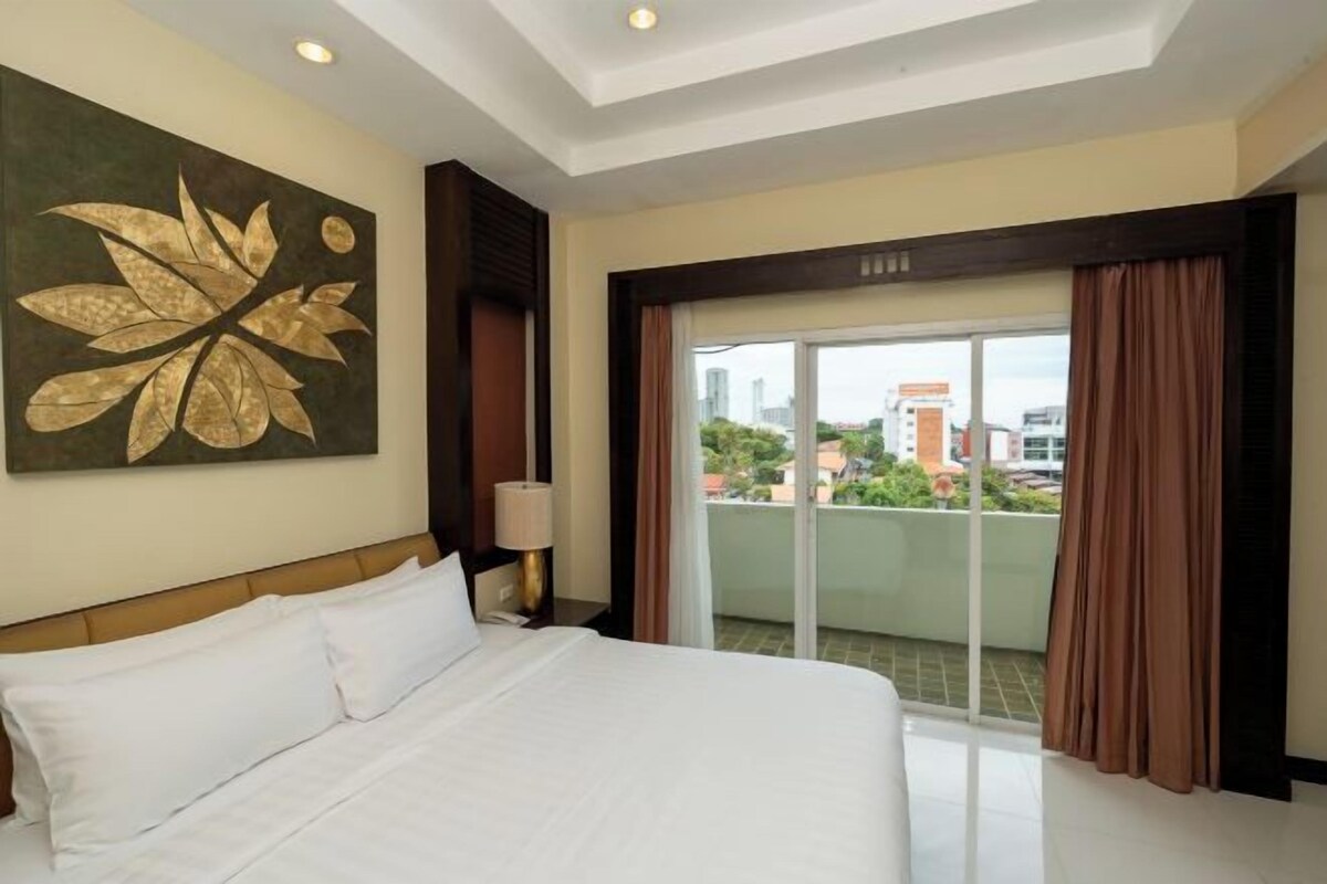 A hotel room with a large bed, a view of the city through a balcony, and a decorative wall piece.