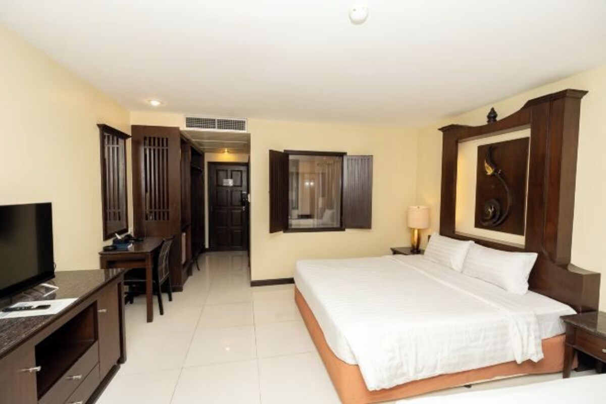 Una habitación de hotel con cama, escritorio, televisor y ventana con cortinas.
