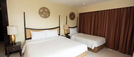 Quarto de hotel com duas camas, uma mesa de cabeceira com abajur e cortina.