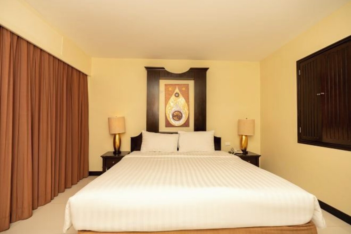 Habitación de hotel con una cama grande, dos mesitas de noche con lámparas, una obra de arte colgada en la pared y una ventana con persianas.