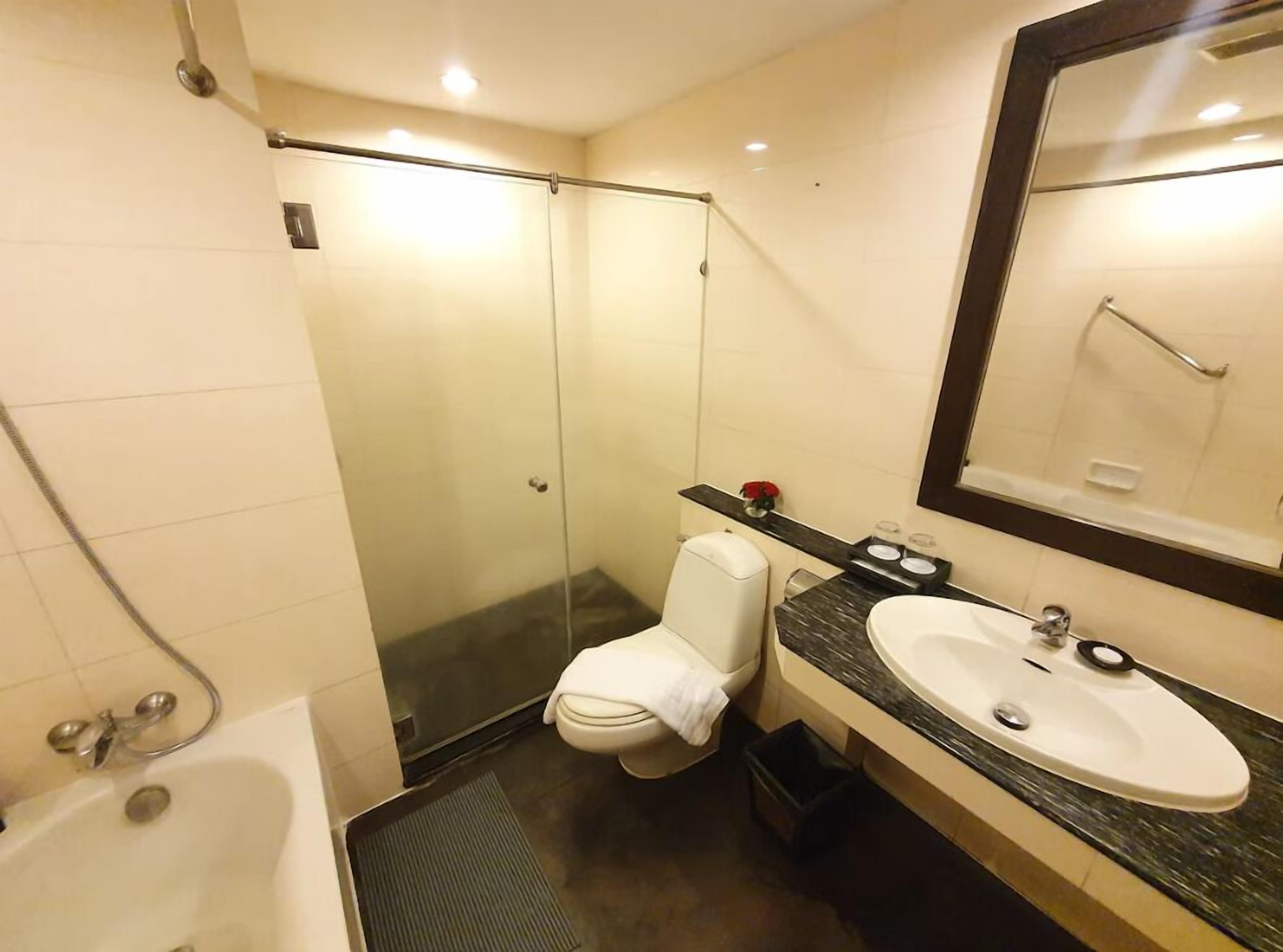 A modern bathroom with a glass shower enclosure, a white toilet, a bathtub, and a vanity with a sink and mirror.