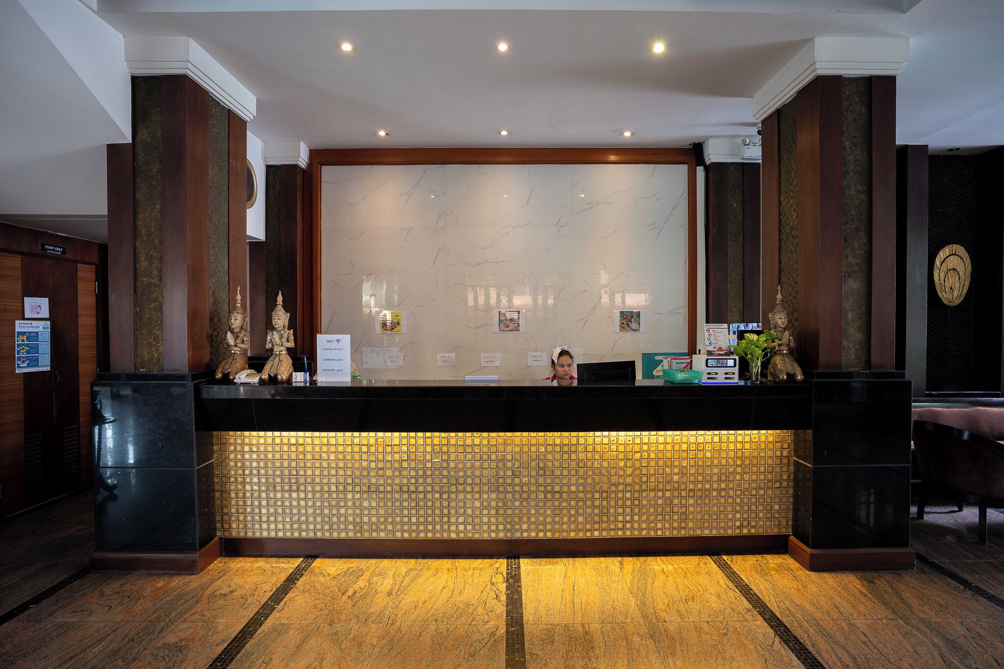 A reception desk with a marble wall, wooden paneling, and a tiled floor.