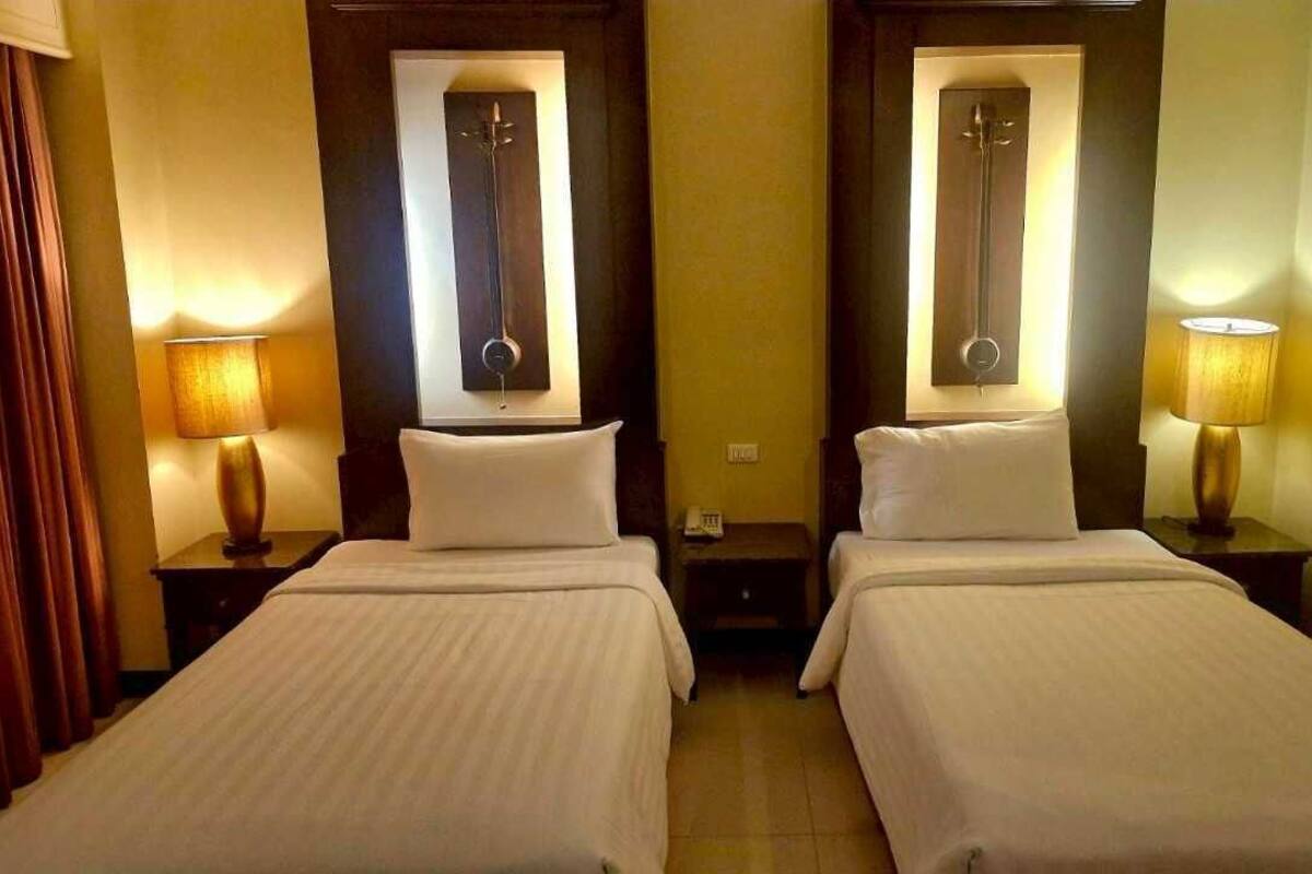 Een hotelkamer met twee bedden, elk met een nachtkastje en een lamp. Boven de bedden hangen spiegels en aan de linkerkant is een gordijn.