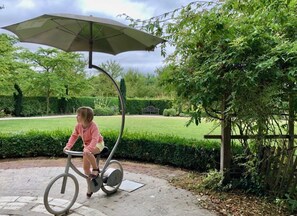 Una persona pedaleando una bicicleta estática bajo una cubierta en un jardín.