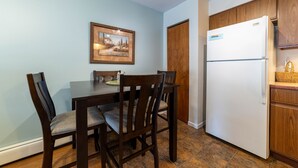 A dining area with a table and chairs, a refrigerator, wooden cabinets, and a framed picture on the wall. - Hidden Gem in Walloon Village (Walloon Lake)