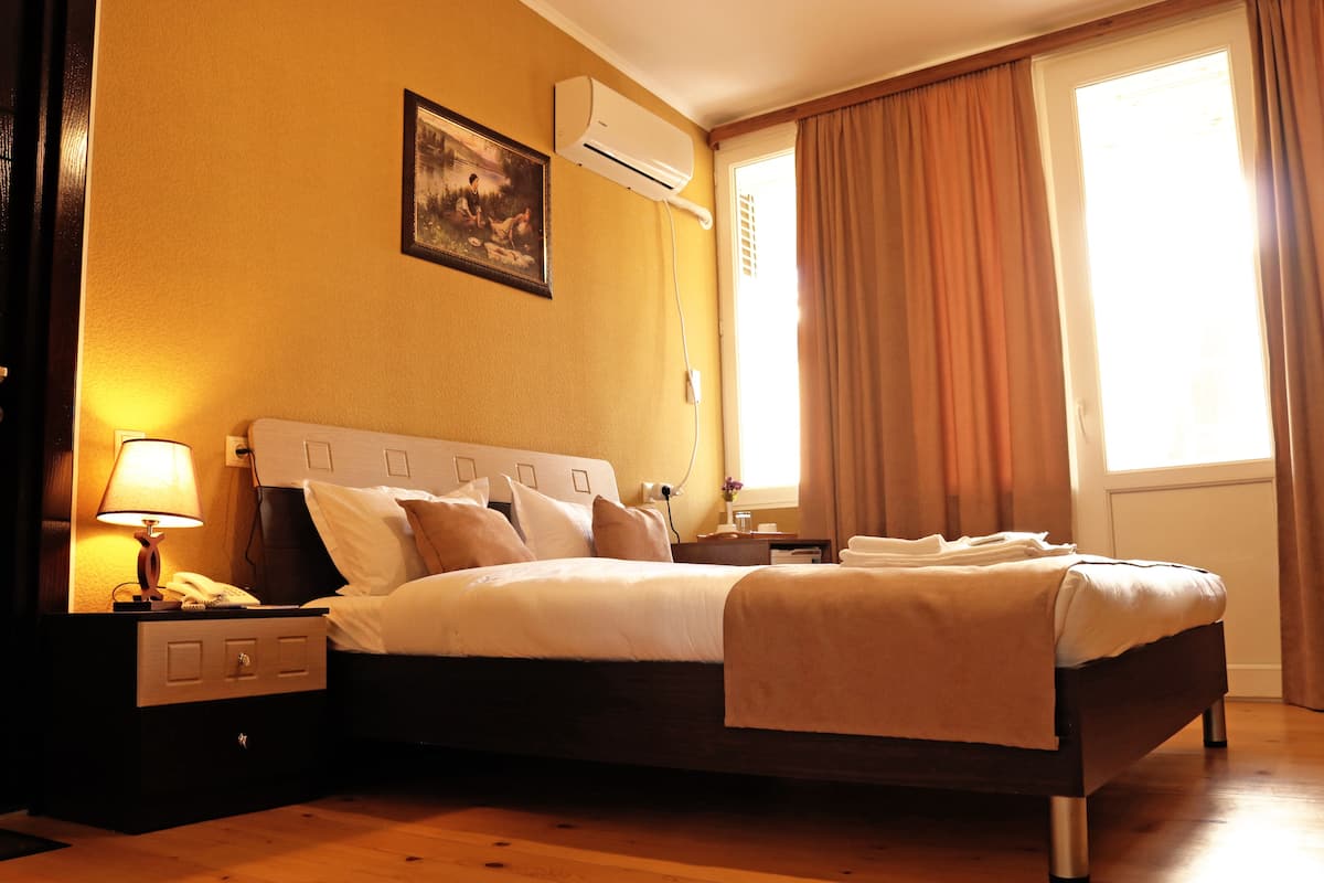 A neatly made bed in a hotel room with a headboard, a bedside lamp, and a nightstand with a lamp and phone.