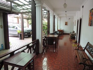 A covered outdoor area with wooden tables and chairs, a bench, and a car parked outside. - Mani Home & Hostel Luang Prabang (Luang Prabang)