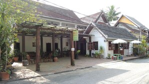 A traditional building with a covered outdoor seating area, potted plants, and a sign indicating a local business.