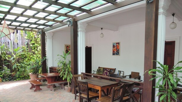 An outdoor patio with a wooden table and chairs, surrounded by potted plants and a brick floor.