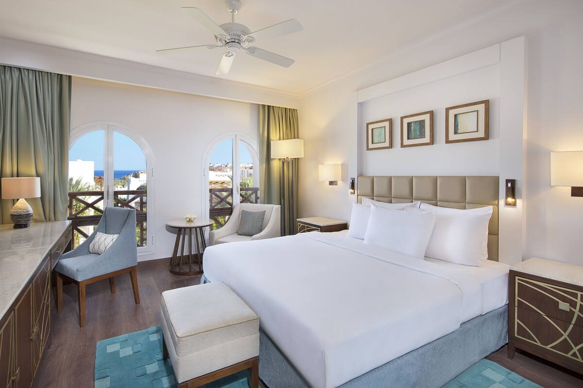 A hotel room with a bed, a desk, a chair, a TV, and a balcony with a view.