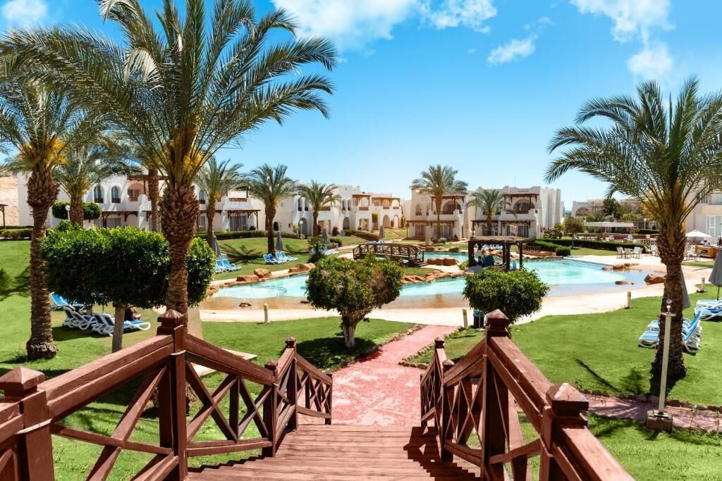 A resort with a pool area, palm trees, and a wooden bridge leading to the pool.