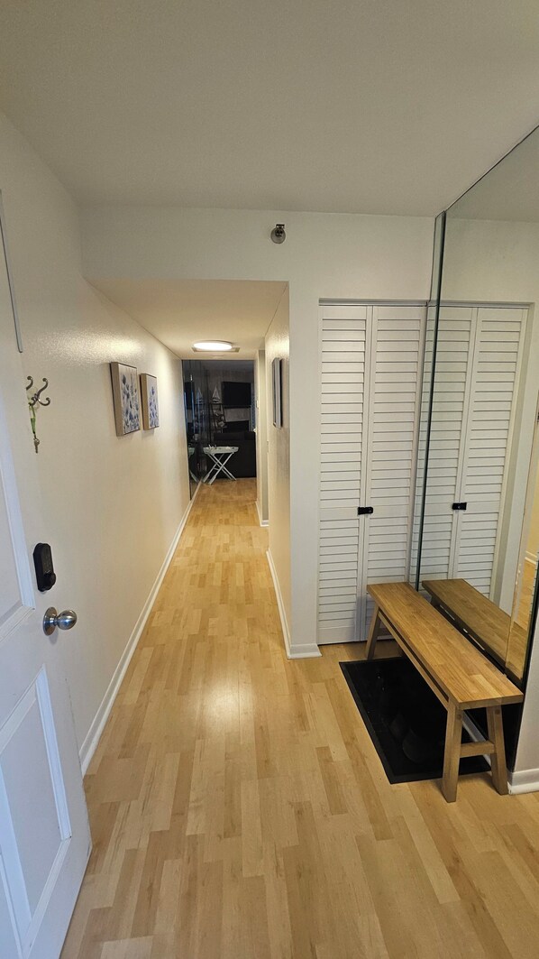 A hallway with wooden flooring, a bench, a mirror, and a set of white doors.